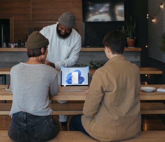 Prinsip Ketika Menghadapi Peperangan Three people sitting on benches at work around a Microsoft laptop