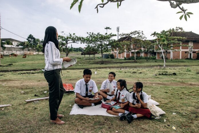 Students in uniforms enjoying an outdoor class with a teacher in a park setting.